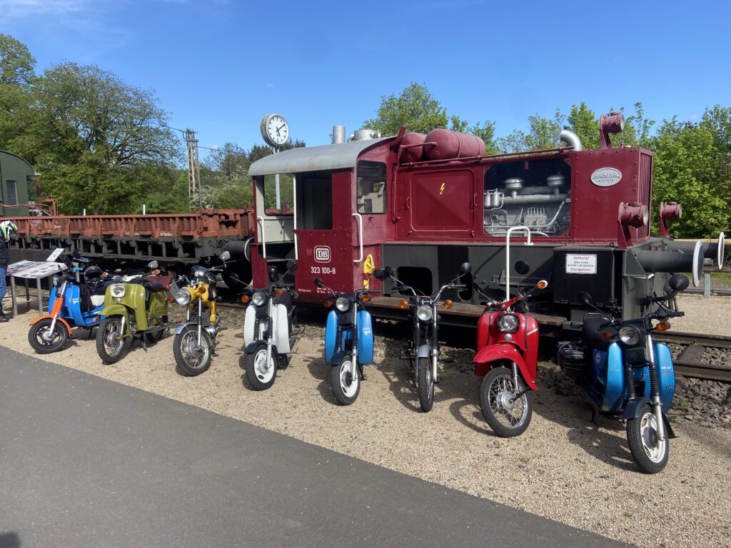 Mehrer Mopeds vor einer alten Lokomotive