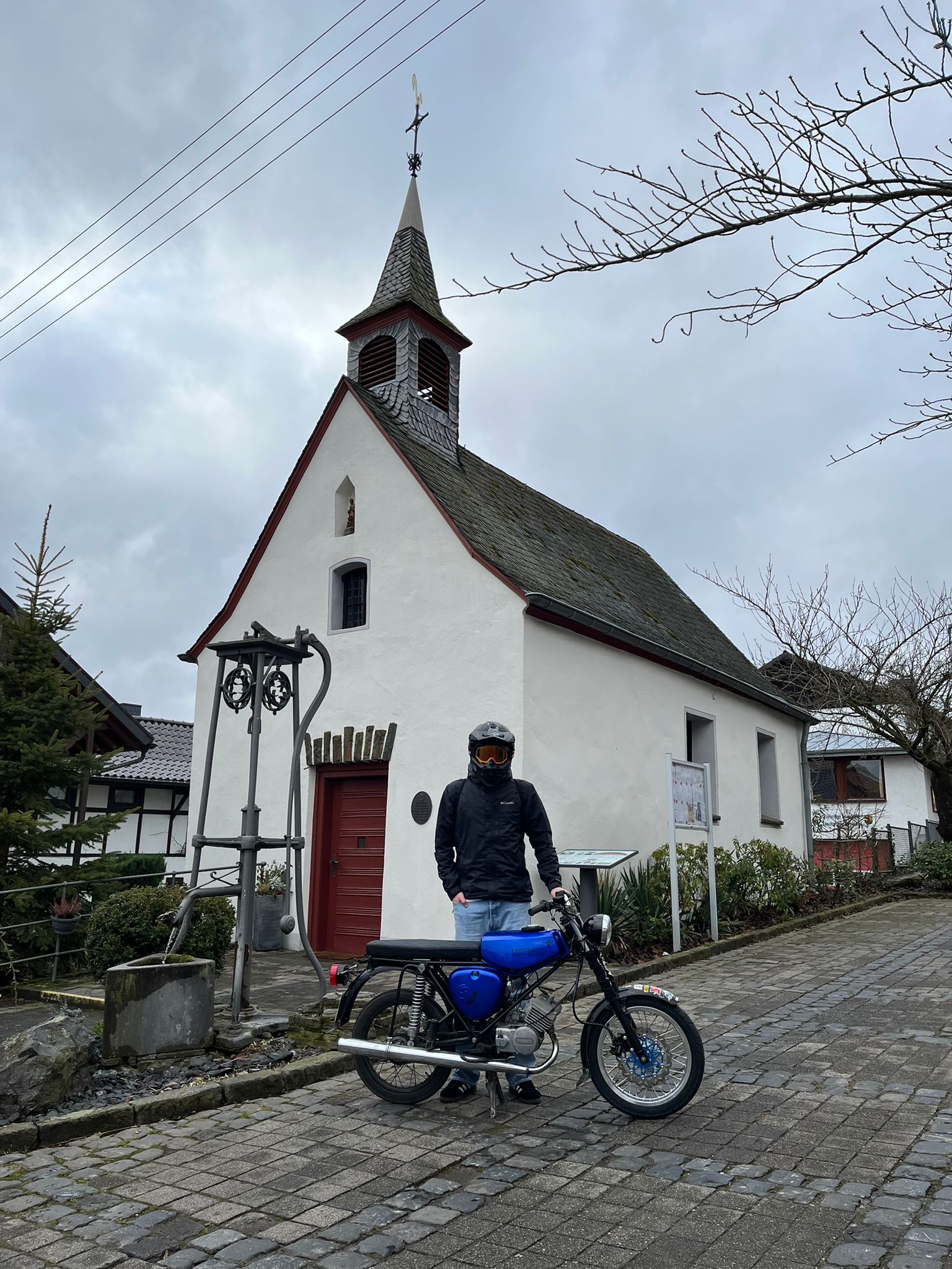 Mann hinter Moped posiert vor Kirche